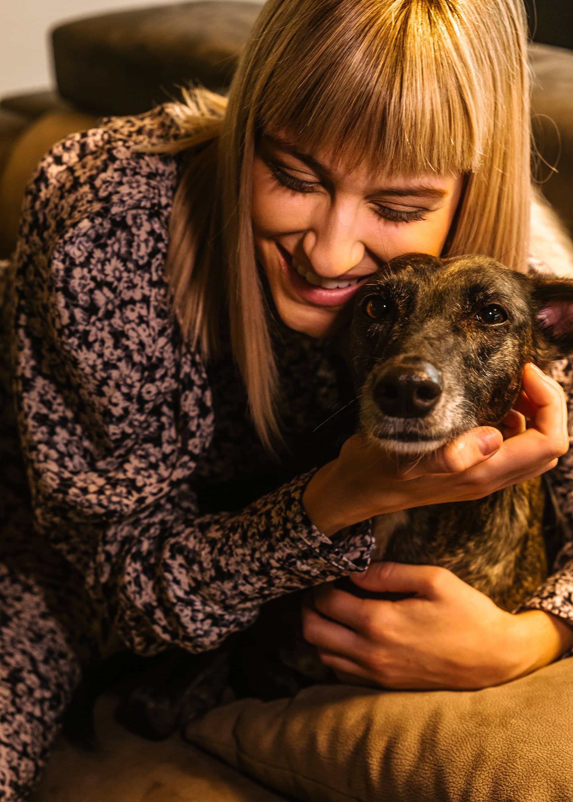 Femme souriante tenant et câlinant un chien à poil court sur un canapé.