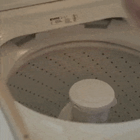 Personne plaçant un lit pour animaux Comfy Wopiloo dans une machine à laver.